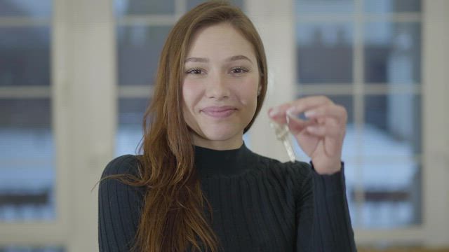 Young woman holds up house key with big smile.