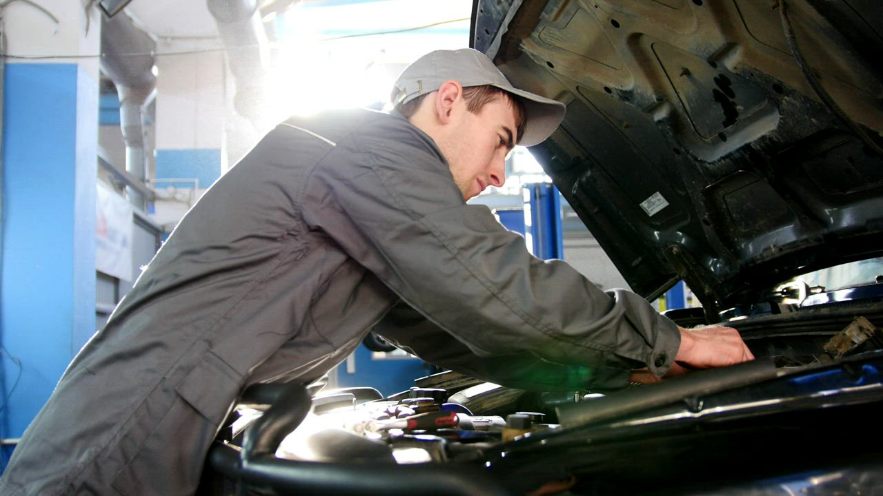 Apprentice mechanic in overalls working under the hood of a vehicle