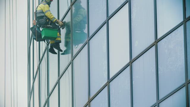 Man hanging on ropes cleaning windows in a building.