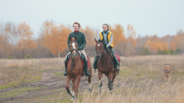 Two women are galloping on the field.