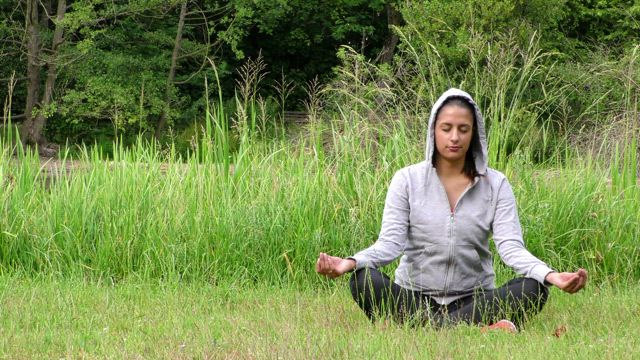 Woman in hoodie meditating on the grass.