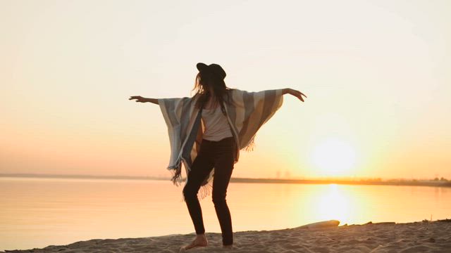 Stylish millennial woman spins on beach at sunset.