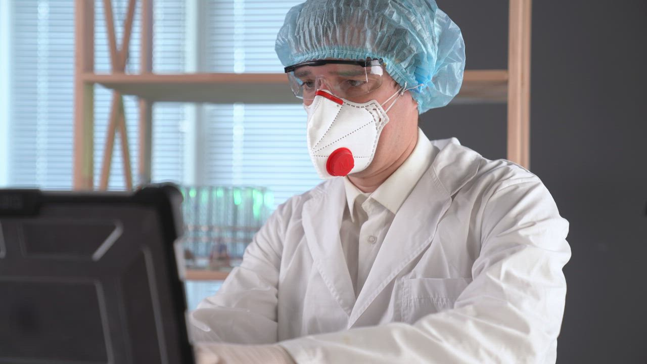 Doctor using a facemask typing on a computer - Free Stock Video