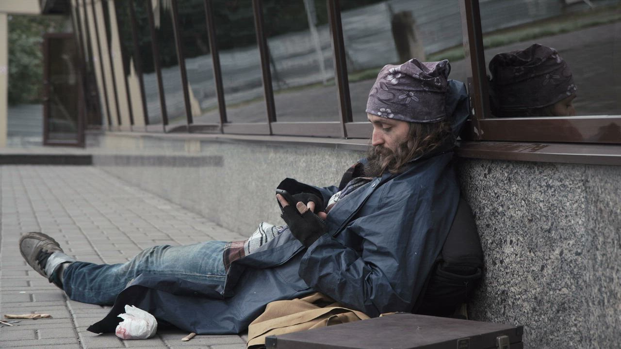 Homeless man checking the mobile phone on the sidewalk - Free Stock Video