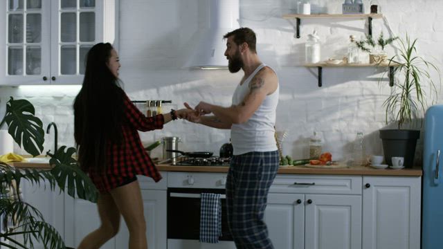 Multiracial couple dancing in the kitchen.