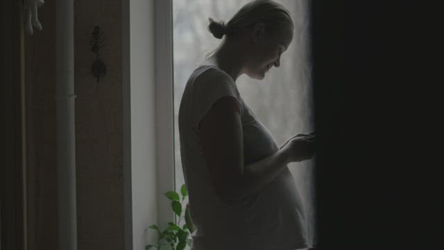 Pregnant woman standing by a window.