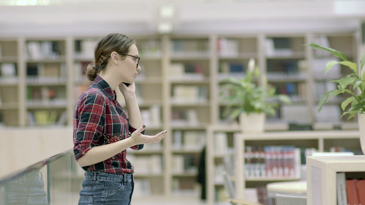 Student woman talking on the phone in the library - Free Stock Video
