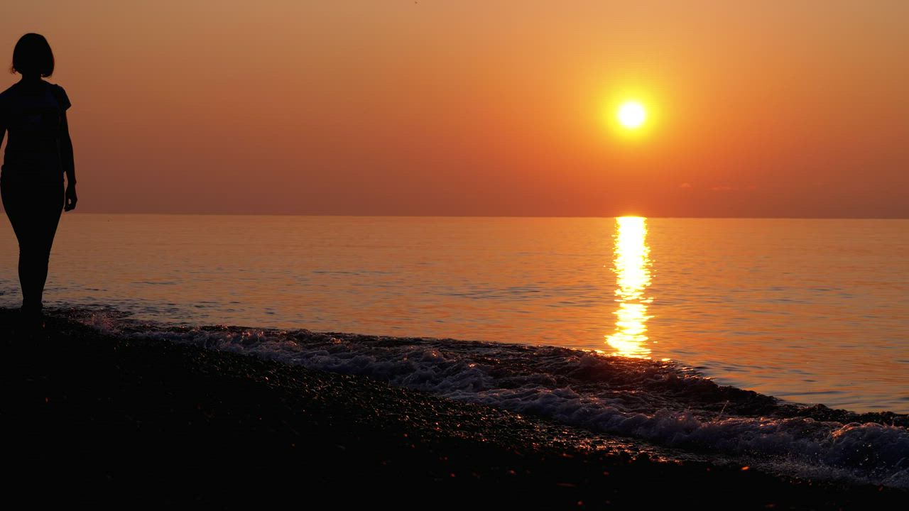 Silhouette of a woman walking along the beach - Free Stock Video