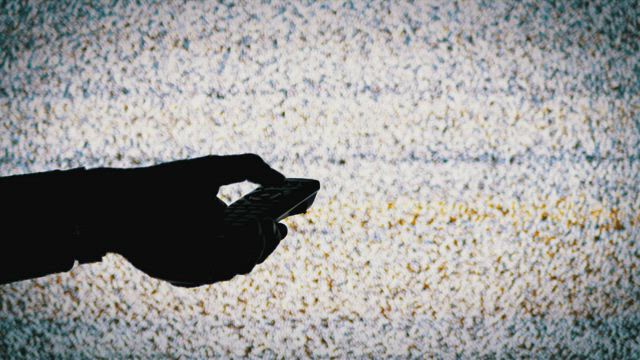 Silhouette of a hand holding a TV remote .