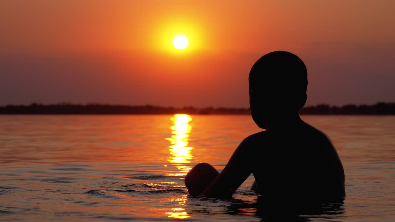 Silhouette of a boy in the sea at sunset - Free Stock Video