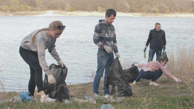 Group of volunteers cleaning up trash near a river.