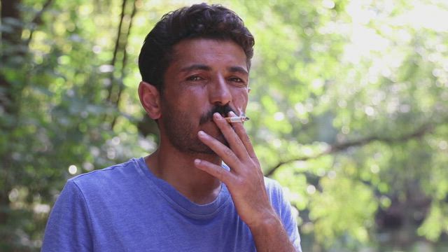 Man smoking outside looking directly to the camera.