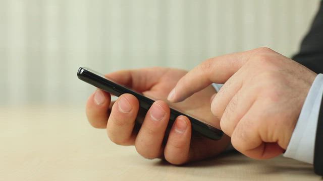 Hands of a man in a suit using his smartphone.