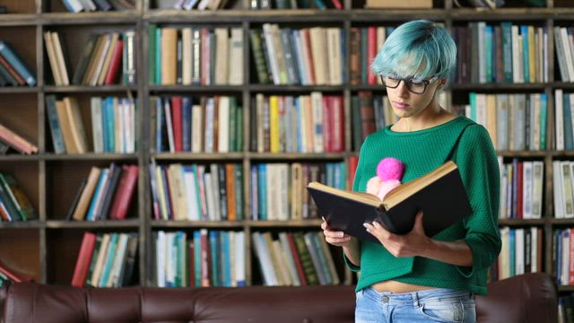 Girl with glasses reading a book in a library.