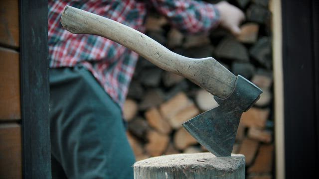 Ax stuck in a log while a lumberjack works.