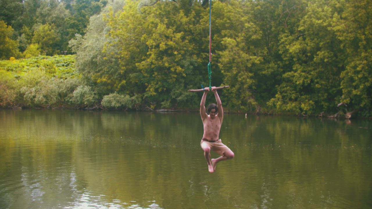 Man jumps into a lake by swinging with a rope - Free Stock Video