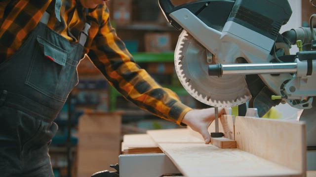 Carpenter slicing a wooden board with a saw.