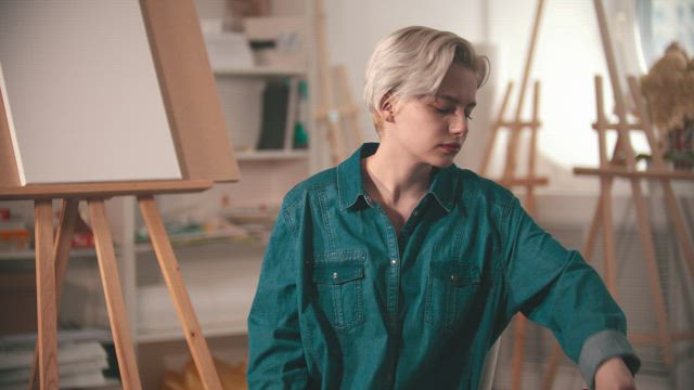 Young female artist checking cans of paint in her studio.
