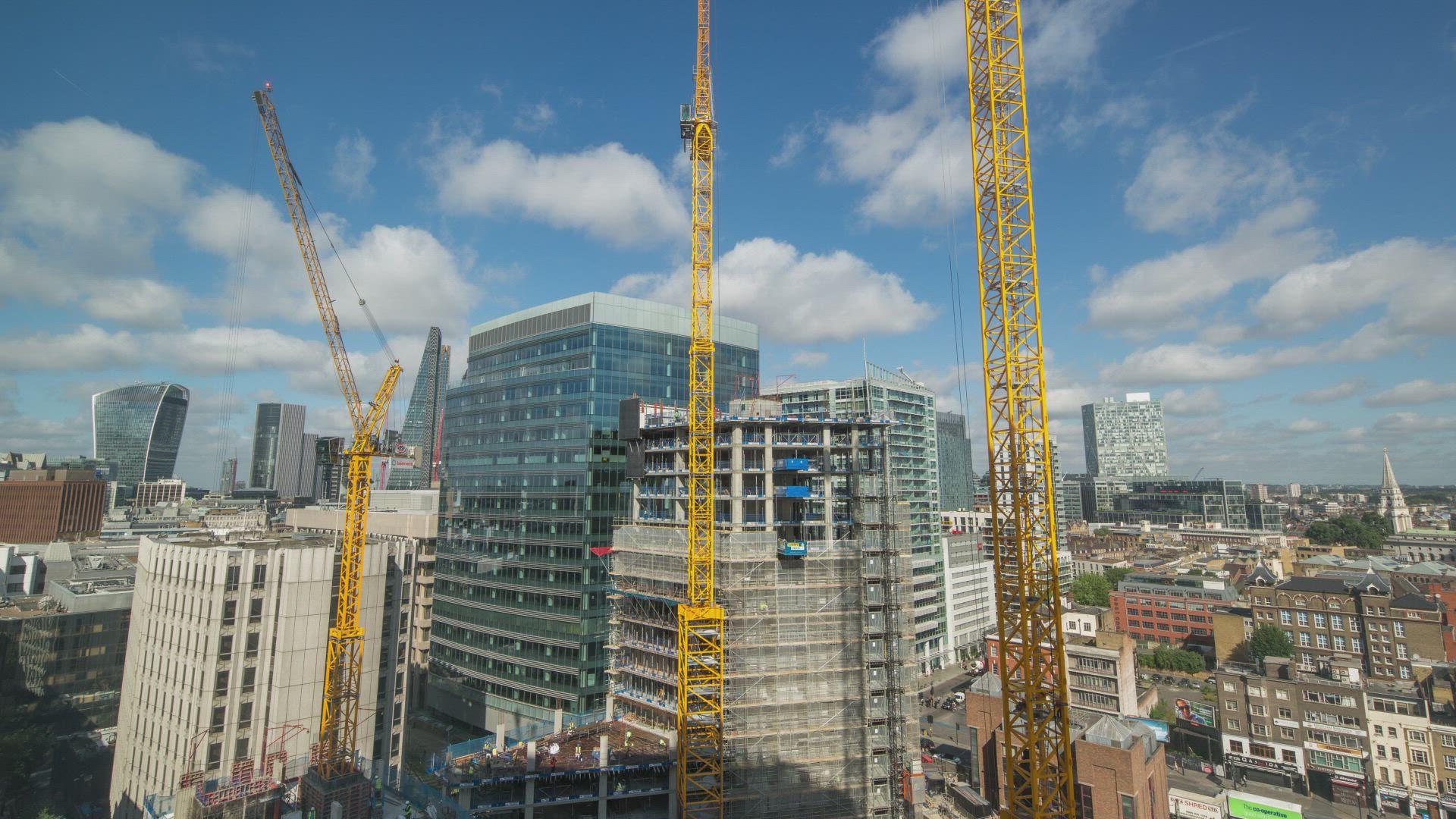 Tower cranes rising above a high-rise construction site against a blue sky