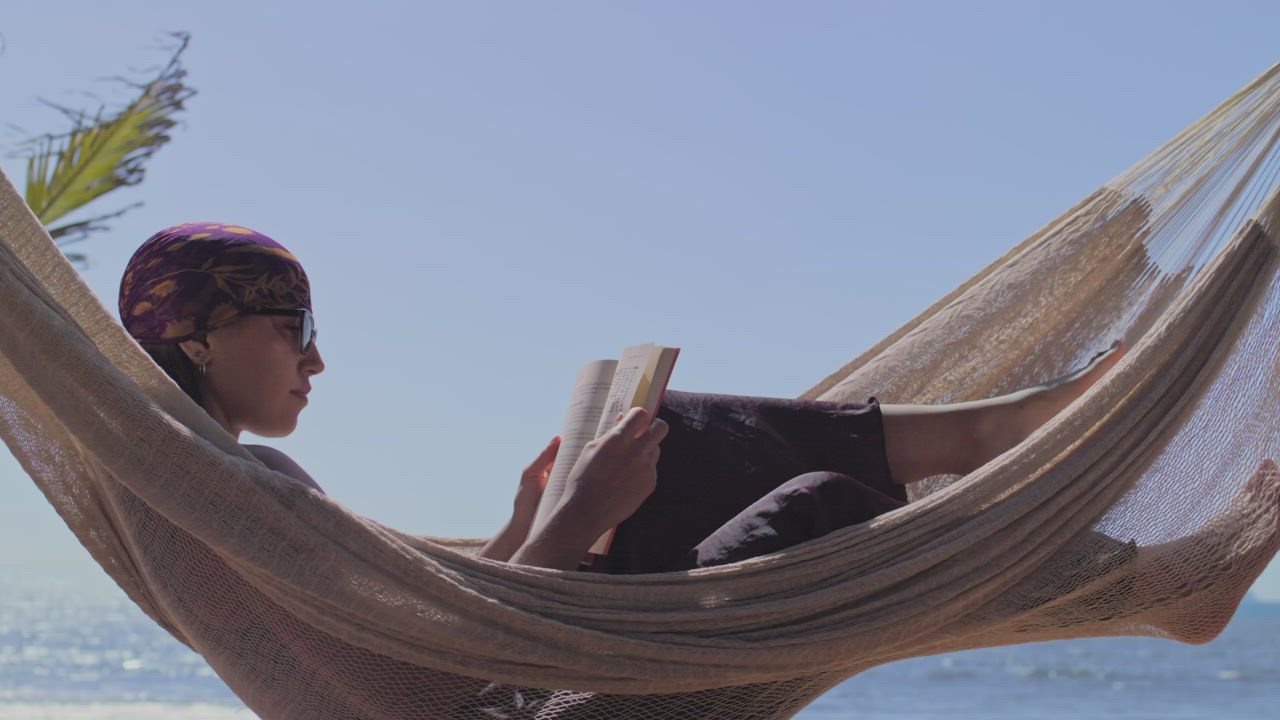 Woman reading lying in a hammock on a sunny beach - Free Stock Video