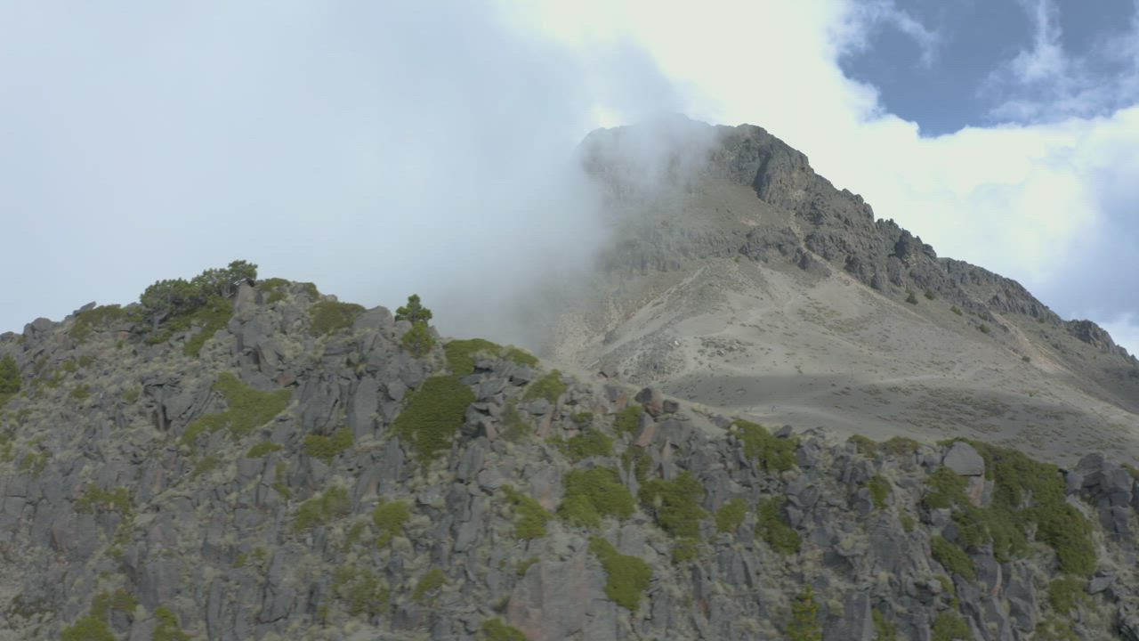 Aerial view of a rocky mountain peak on a foggy day - Free Stock Video