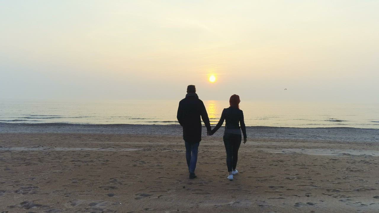 Couple walking on a beach towards the water - Free Stock Video
