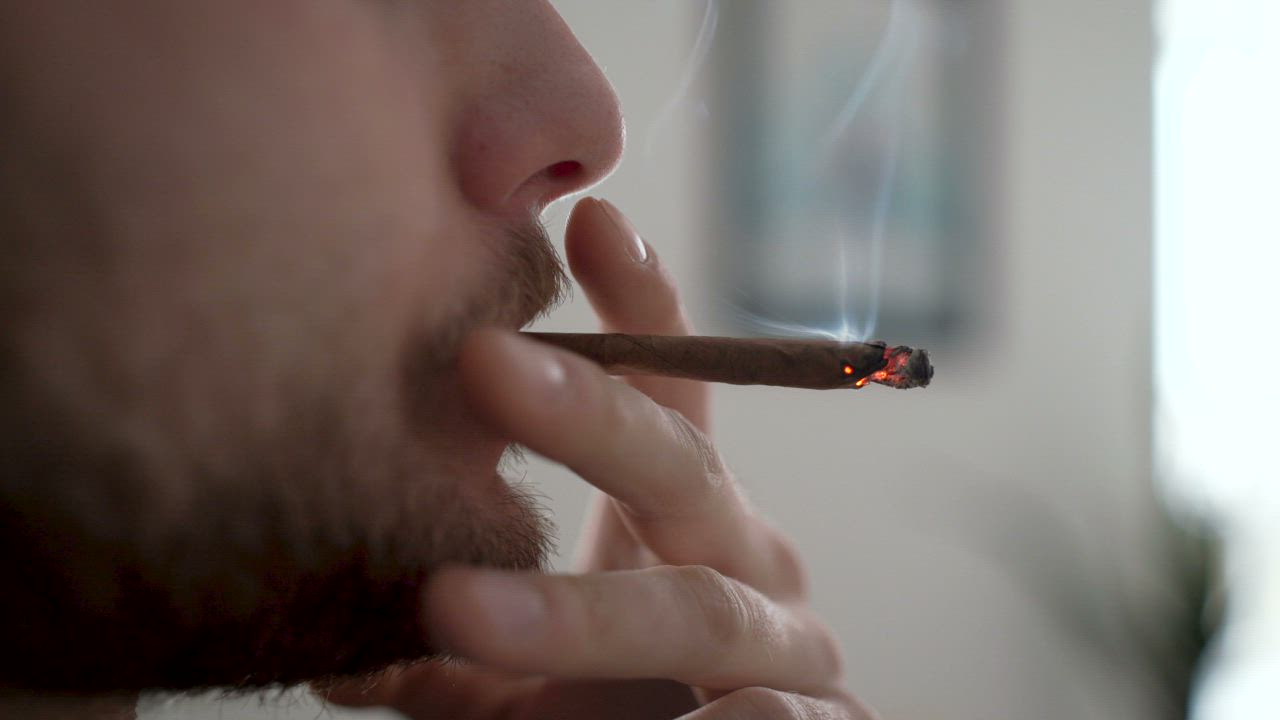 Man with beard smoking a thin cigar indoors