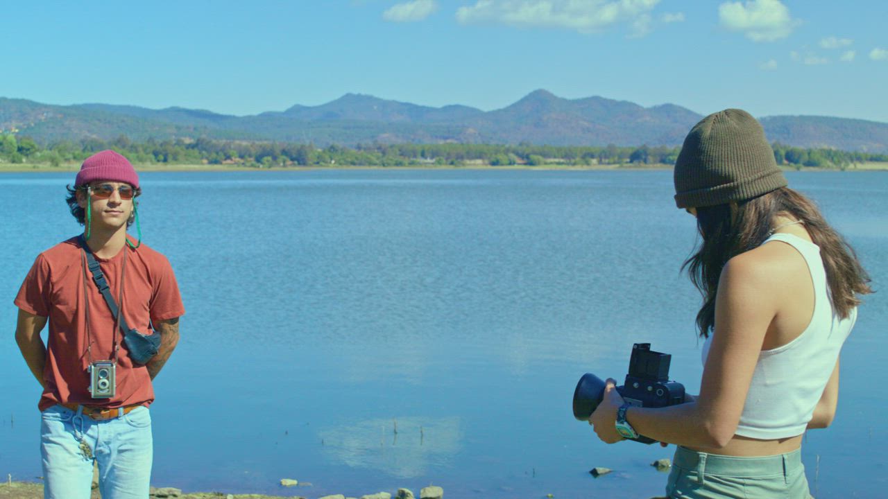 A young photographer give directions to a male model by the lake ...