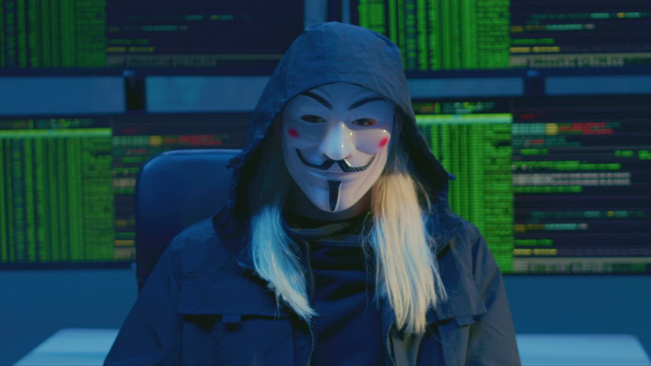 Hooded hacker in front of screens of code
