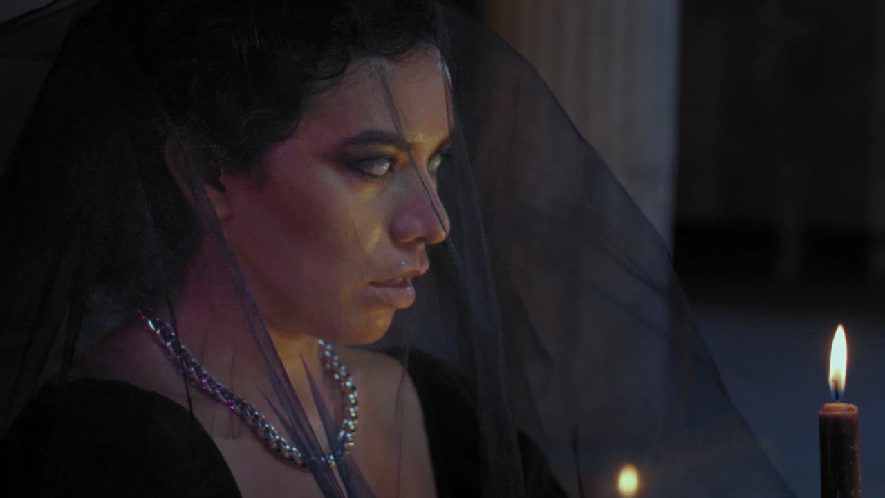 A woman with blind eyes holds a lit candle while she whispers a ritual ...