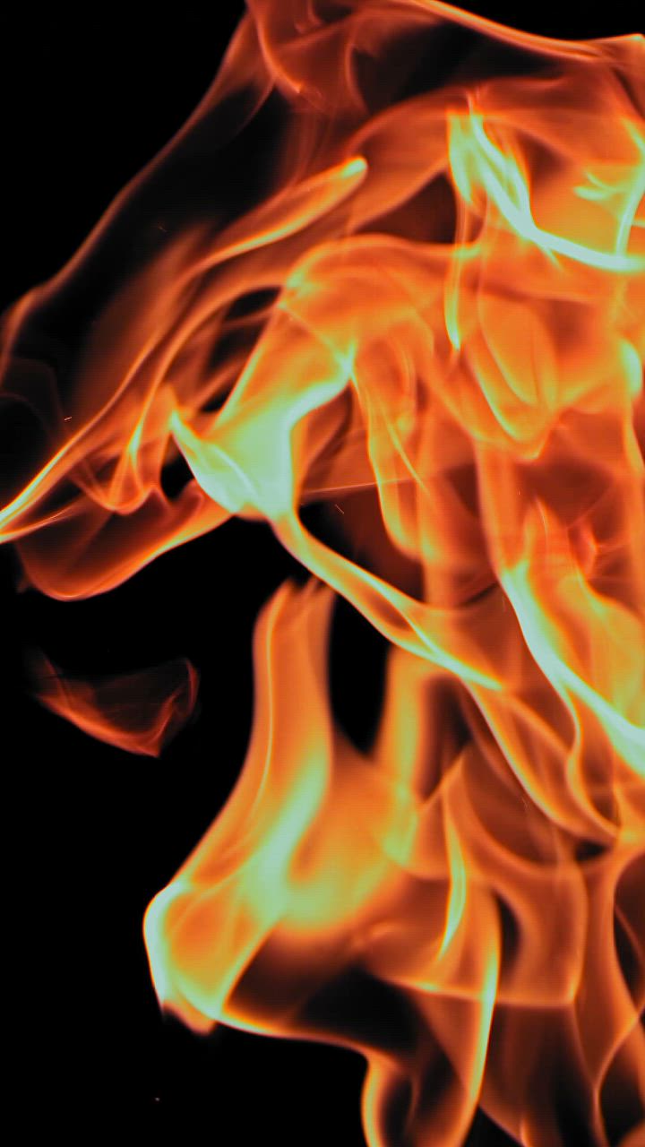 Over a dark background mesmerizing flames flicker and flow upwards ...
