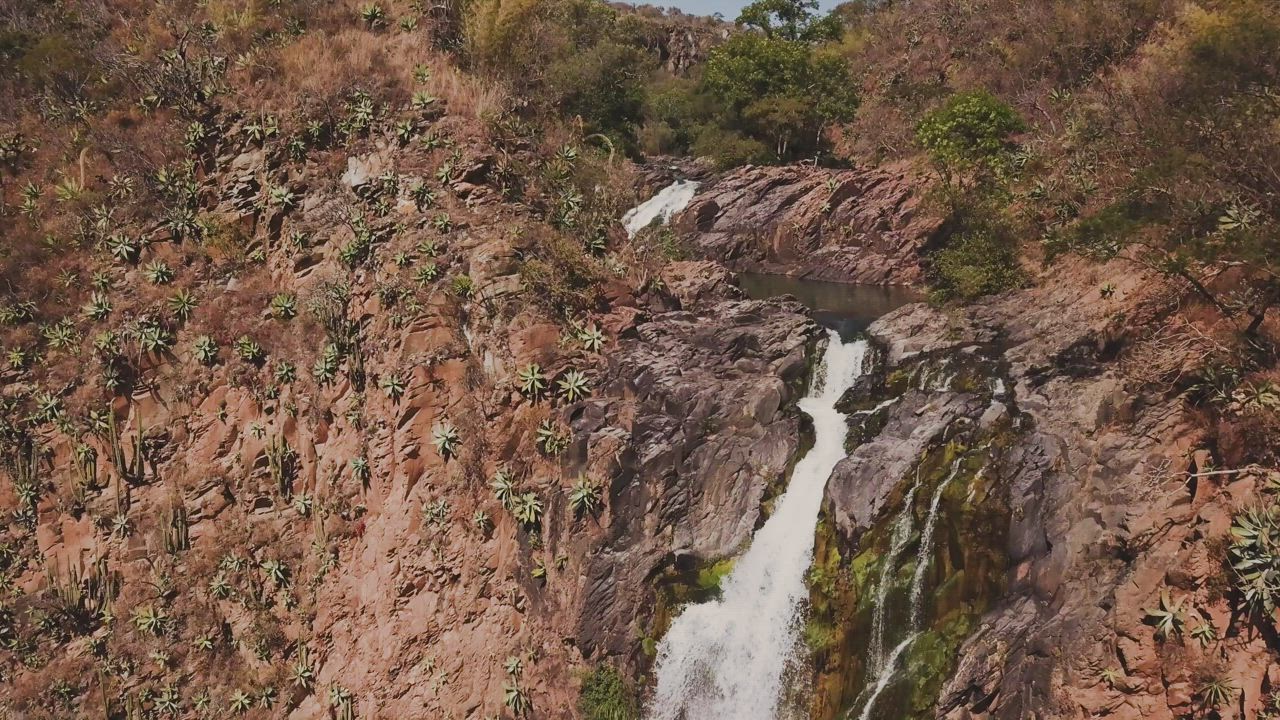 Waterfall over red rocks creating a rainbow - Free Stock Video