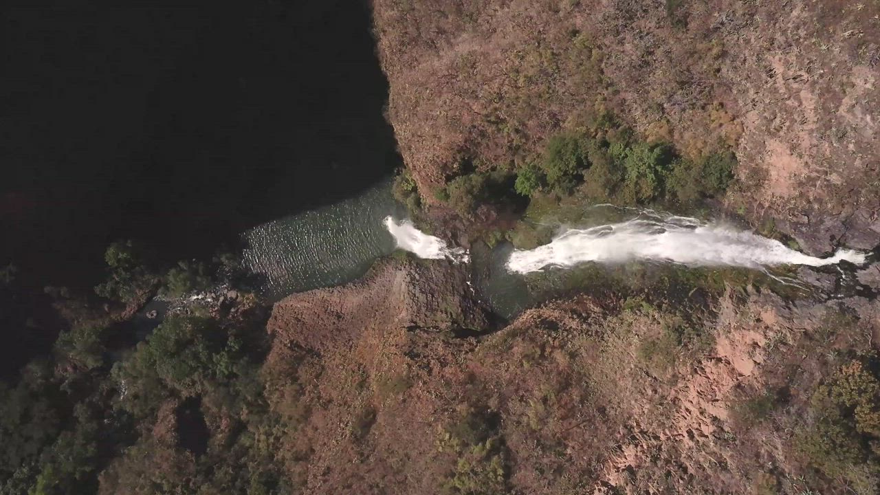 Waterfall between red rocks and trees - Free Stock Video