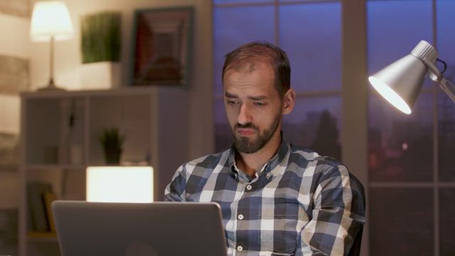 Thinking man works late and stretches in home office.