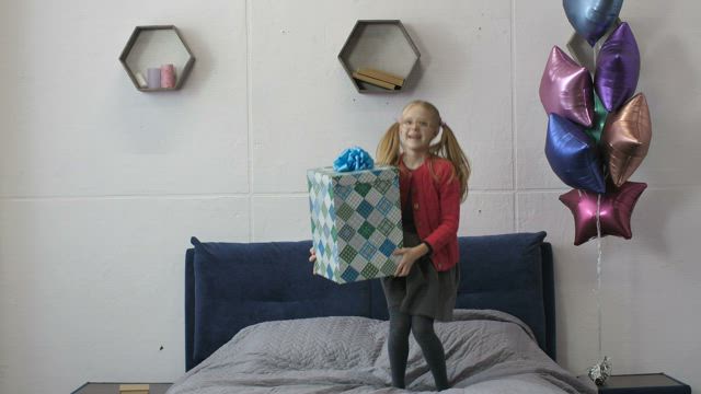 Happy girl jumping on her bed with a gift.