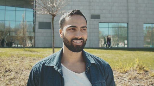 Handsome Arab man smiles at camera outside building.