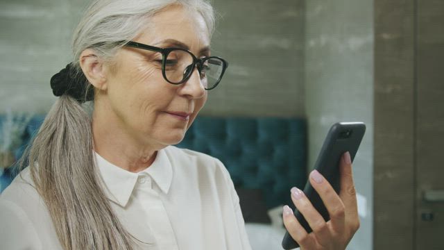 Elderly woman texts on mobile phone and smiles.